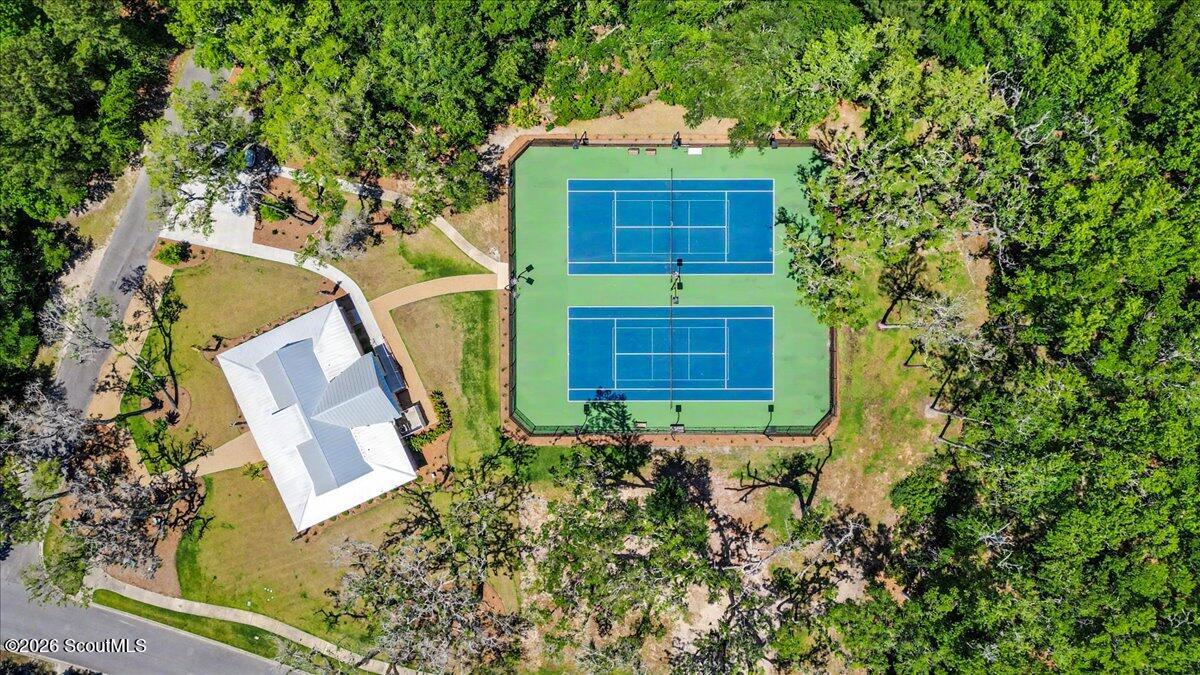 Two blue tennis courts beside a white-roofed pavilion amid mature trees.