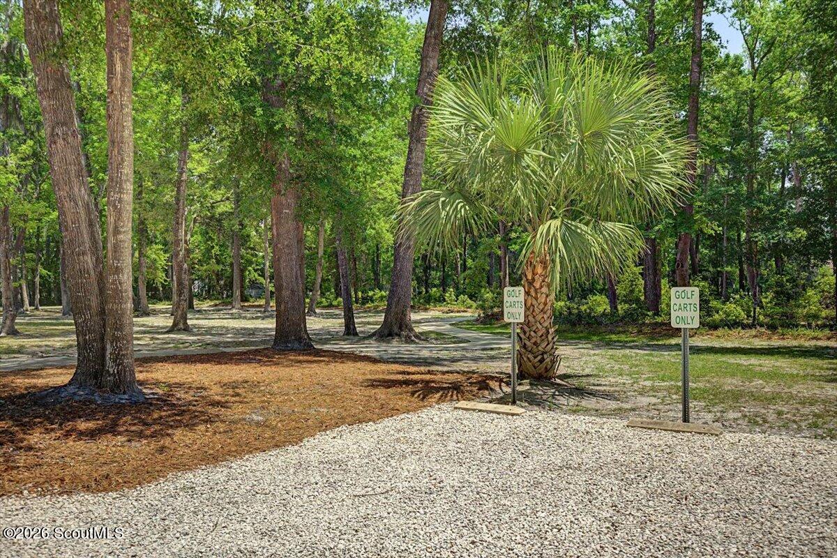 Wooded property beside a gravel golf cart path, with a palm tree and golf cart signs.