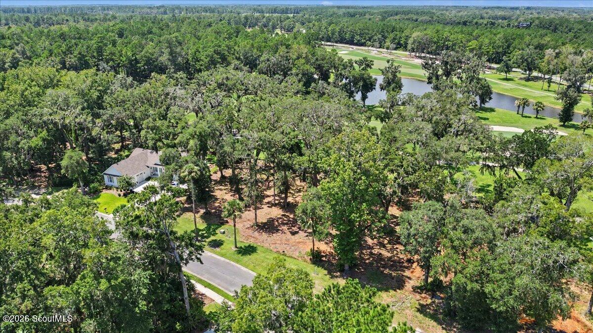 Aerial view of a wooded vacant lot beside a golf course and pond.