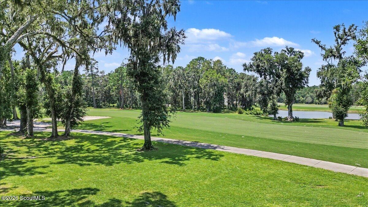 Grassy lot beside a golf course, with moss-draped oaks, a paved path, and a pond.