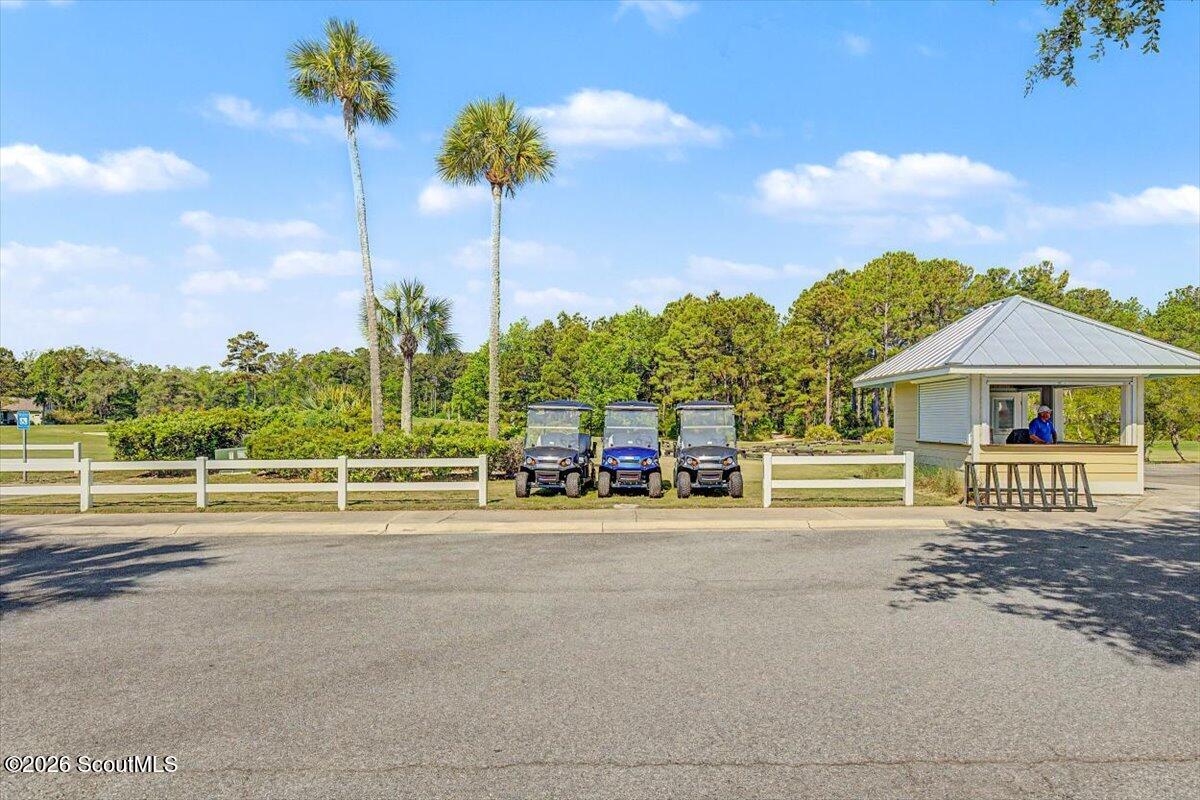 Community entrance with a white fence, three golf carts, and a small guard kiosk.