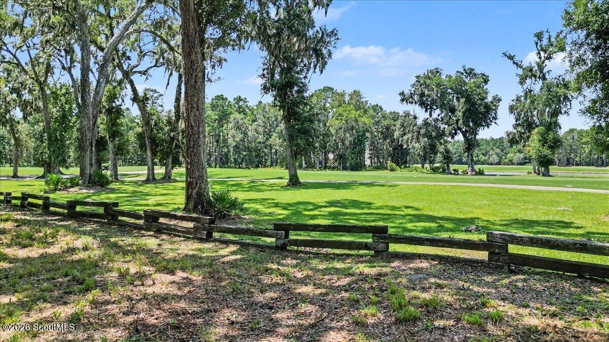 Grassy lot with mature moss-draped trees, a wooden rail fence, and a paved path.