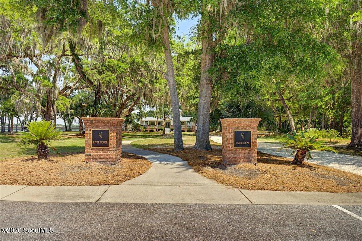 River House entrance with brick sign pillars, a curving walkway, and moss-draped trees.