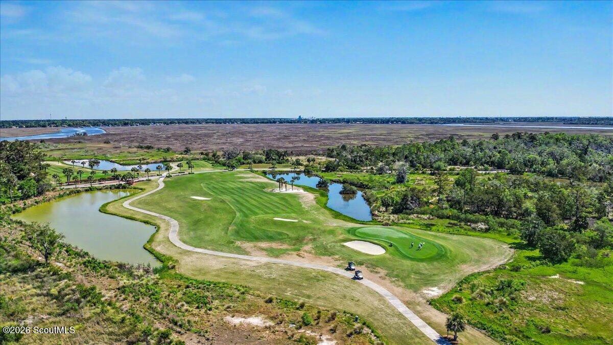 Aerial view of a golf course beside marshland, with water hazards and winding cart paths.