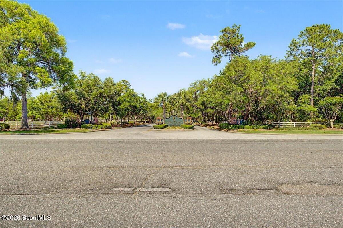 Landscaped neighborhood entrance with a monument sign, white fences, and mature trees.
