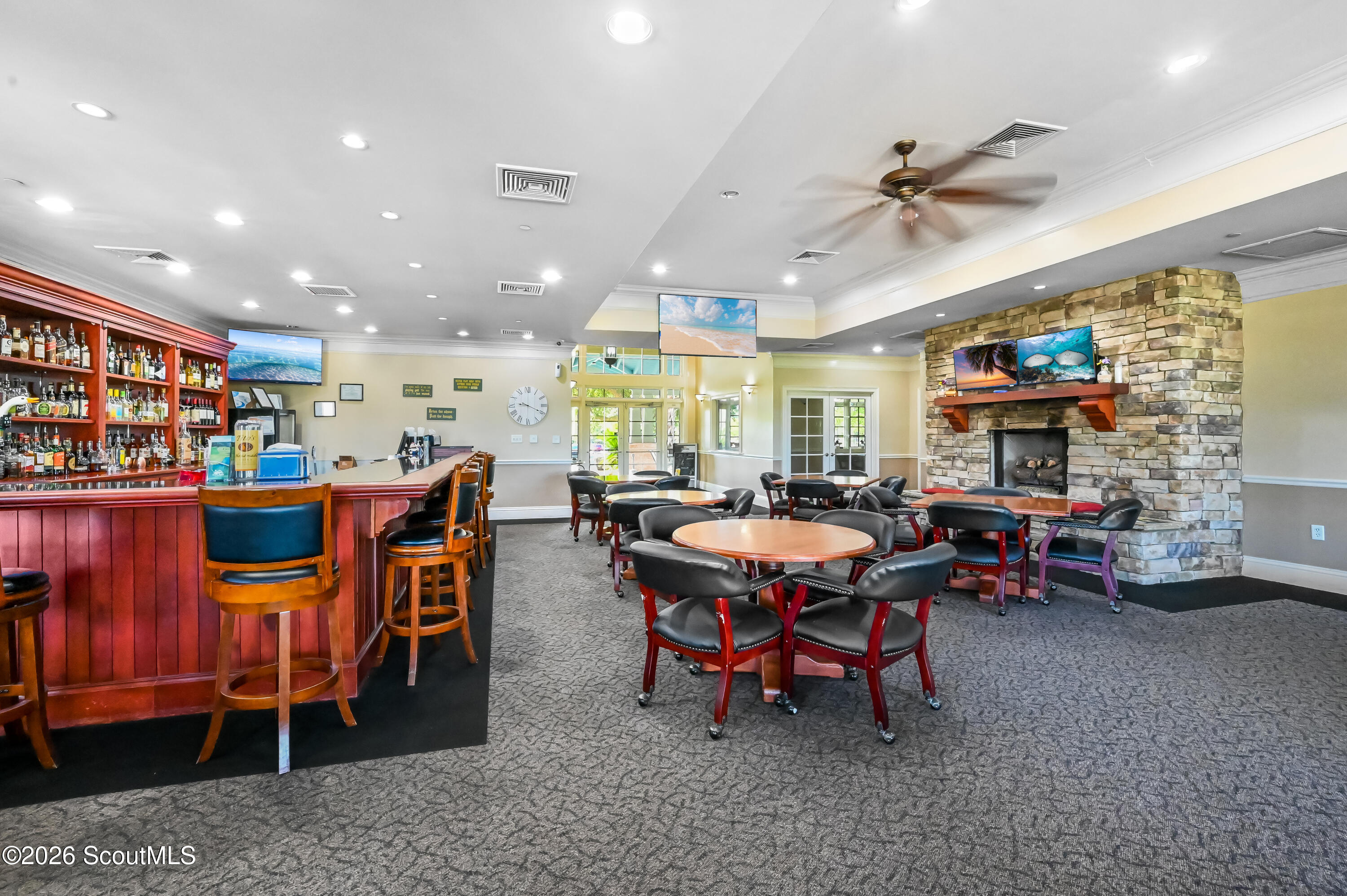 Community lounge with a red wood bar, round tables, and a stone fireplace.