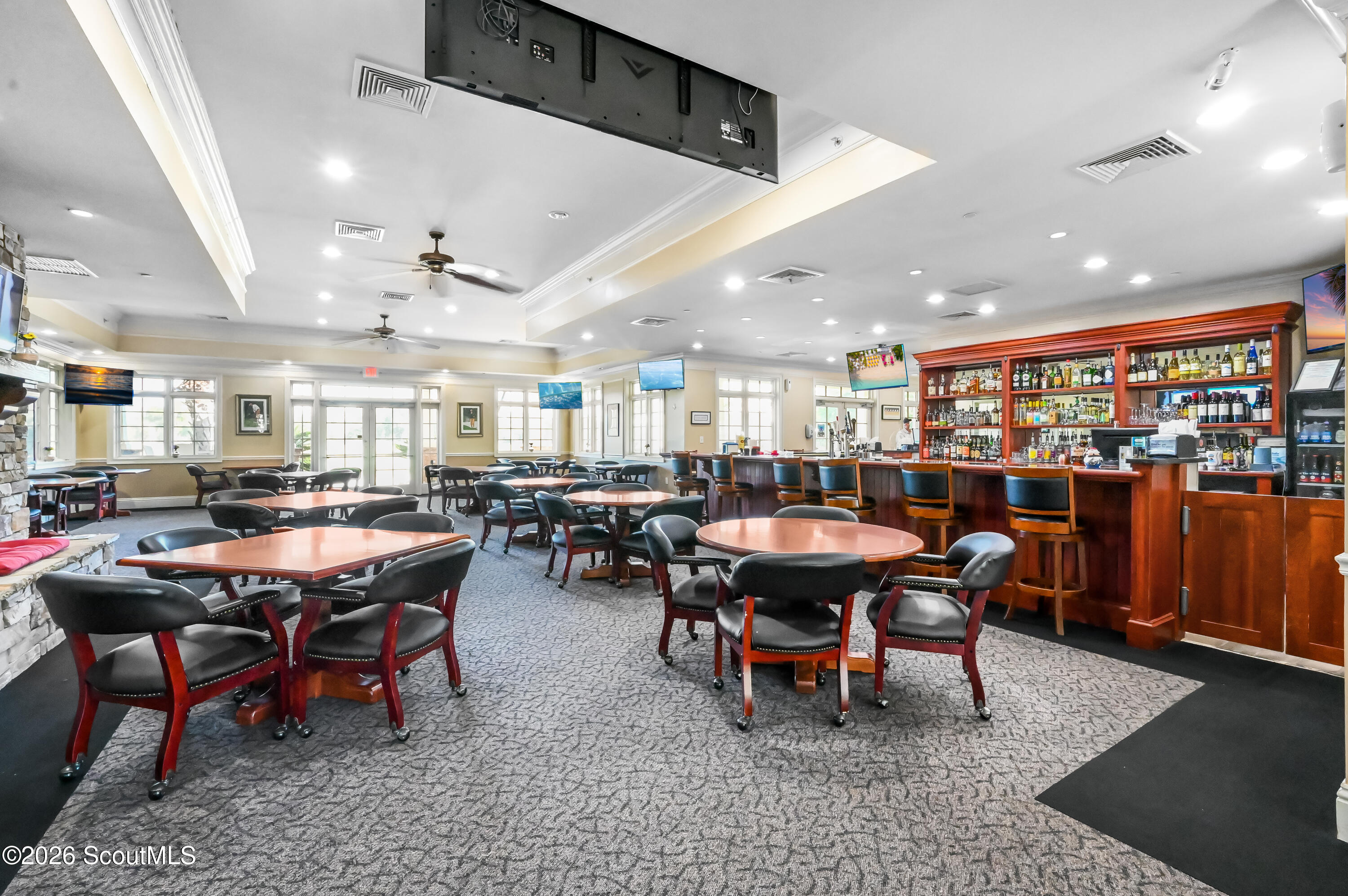 Clubhouse dining room with a stocked wood bar, rows of tables, large windows, and a stone fireplace.