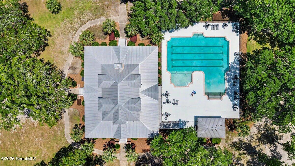 Aerial view of a gray-roofed building beside a turquoise lap pool and landscaped grounds.