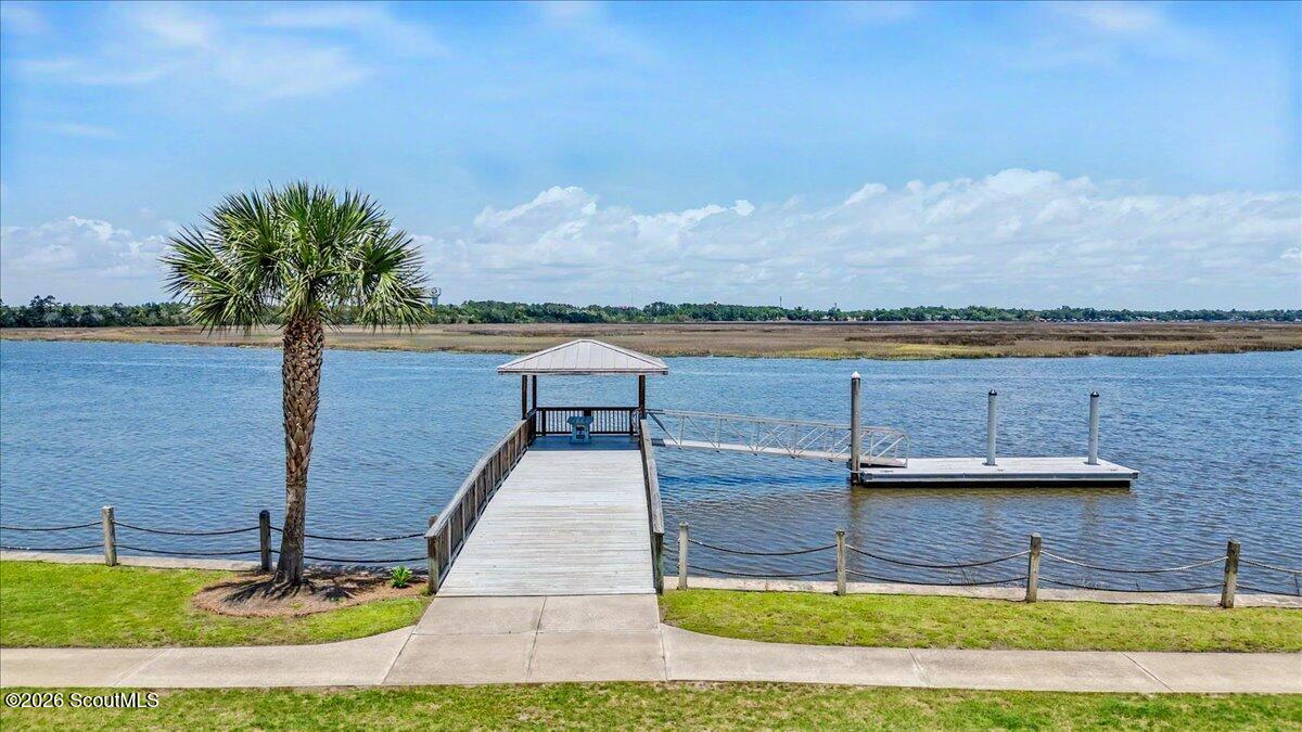 Waterfront dock with a covered pavilion, floating slip, palm tree, and marshland across the water.