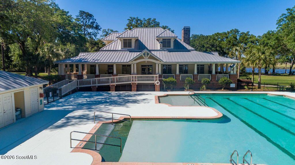 Outdoor swimming pool in front of a two-story clubhouse, with a broad deck and accessible ramps.
