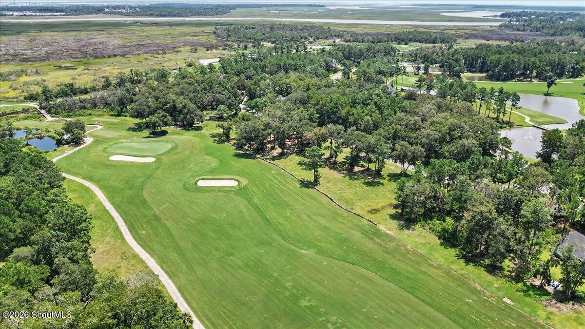 Aerial view of a golf course with sand bunkers, wooded areas, ponds, and distant marshland.
