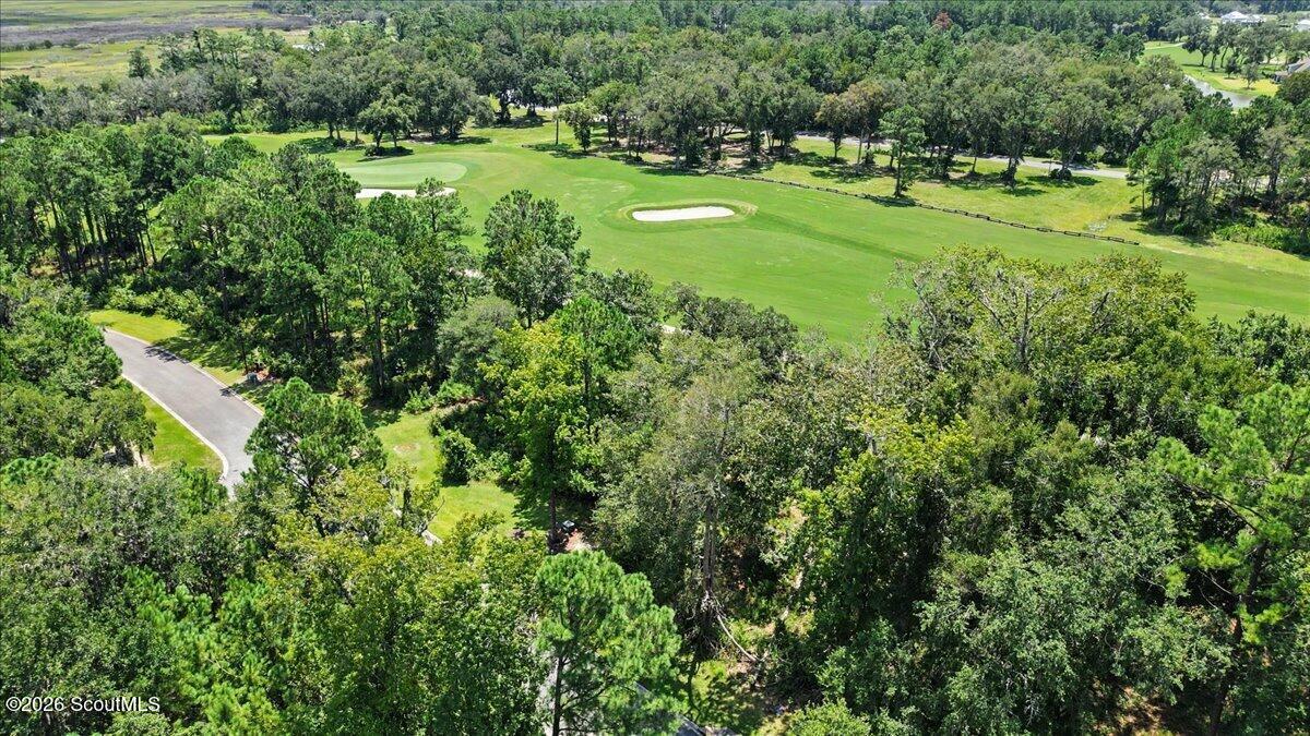 Wooded vacant lot beside a golf course, with a curved road and sand bunker.