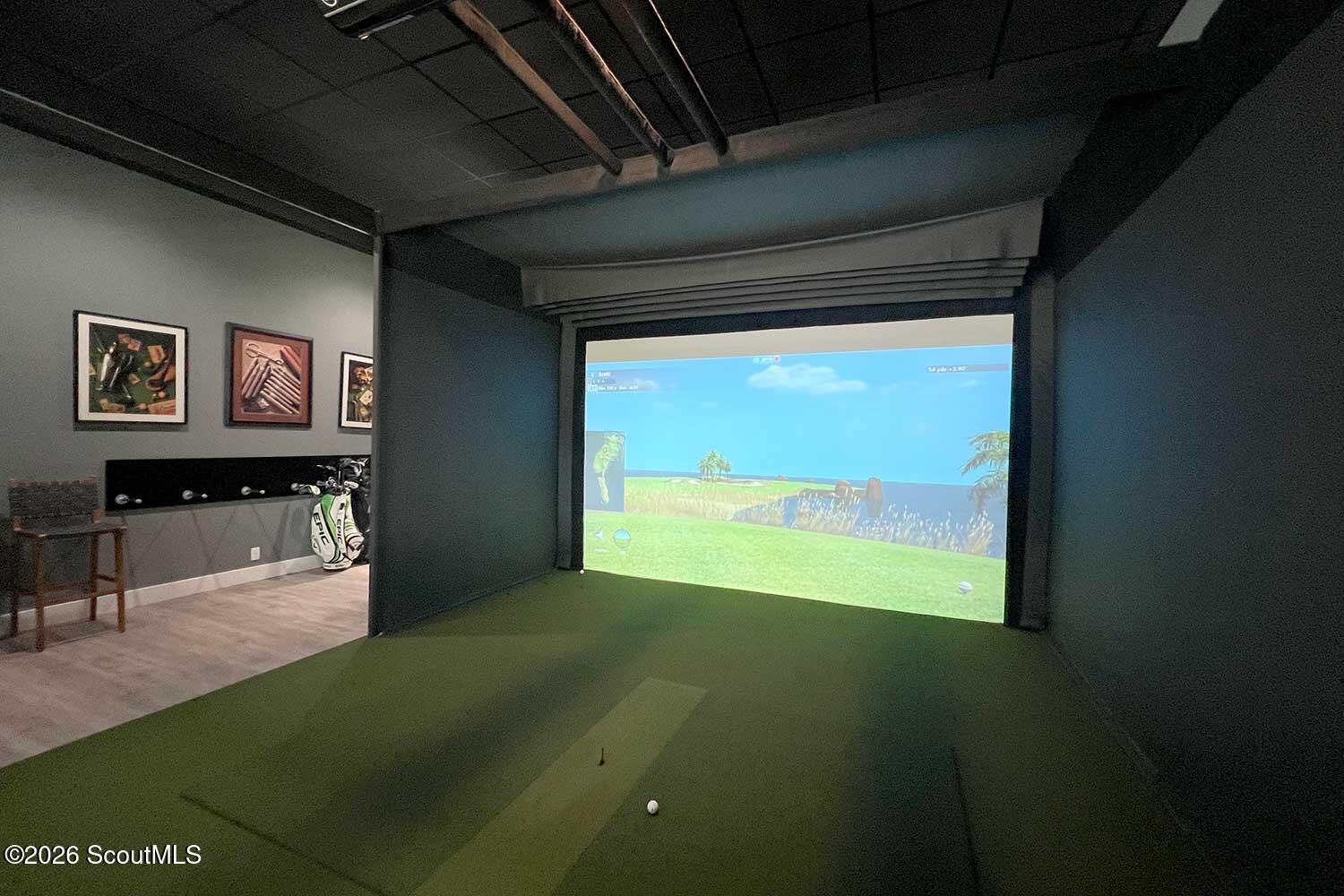 Indoor golf simulator room with putting turf, a large projection screen, and golf bags.