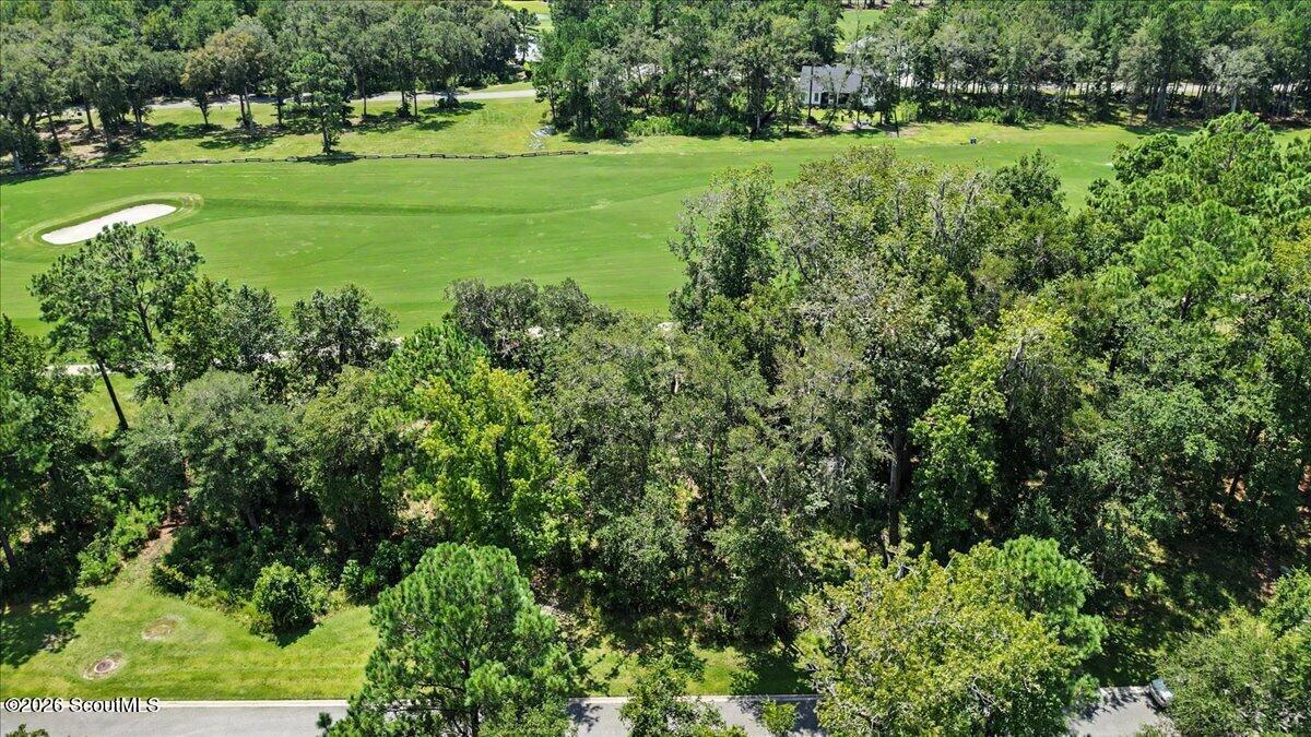 Aerial view of a wooded lot beside a golf course fairway, with a sand bunker and road nearby.
