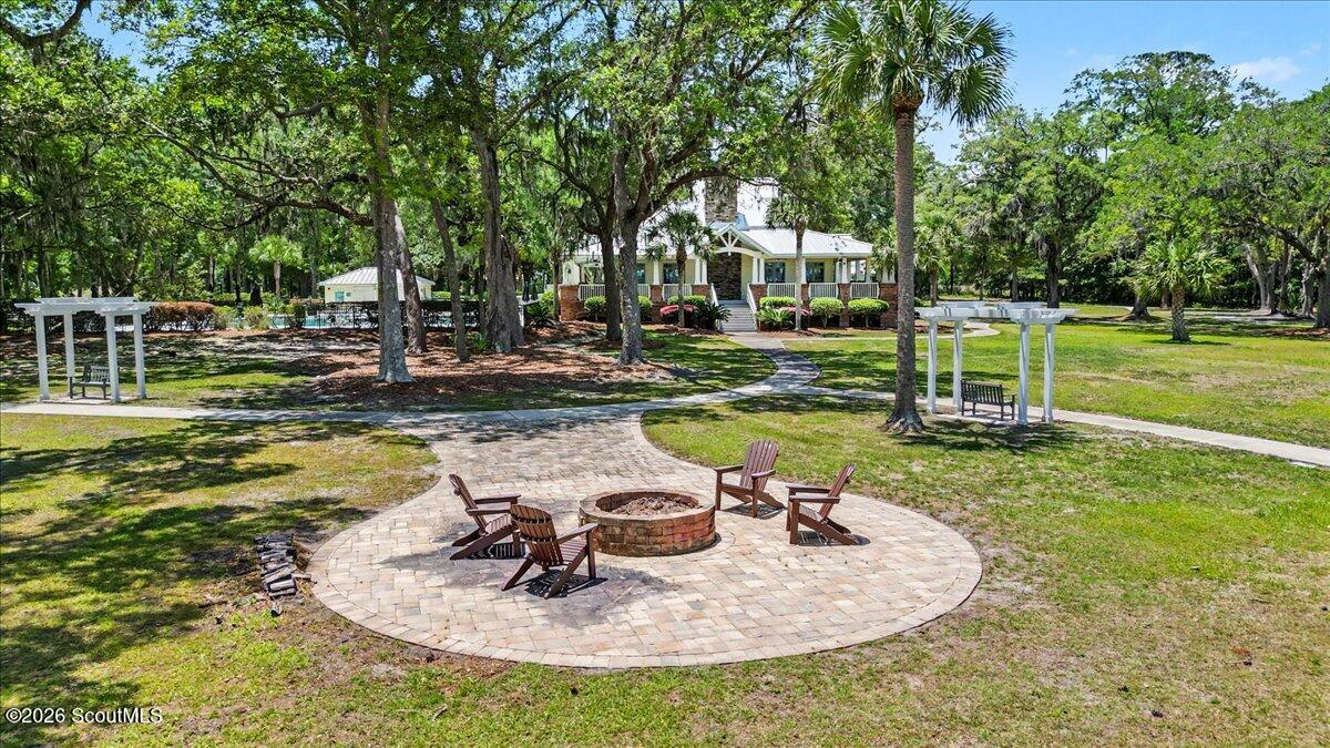 Landscaped courtyard with a circular fire pit, Adirondack chairs, and a home beneath mature trees.