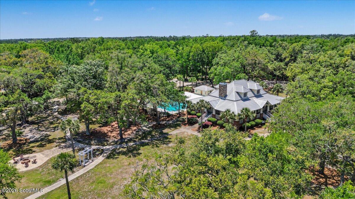 Aerial view of a wooded property with a large building, swimming pool, walking paths, and outdoor seating.