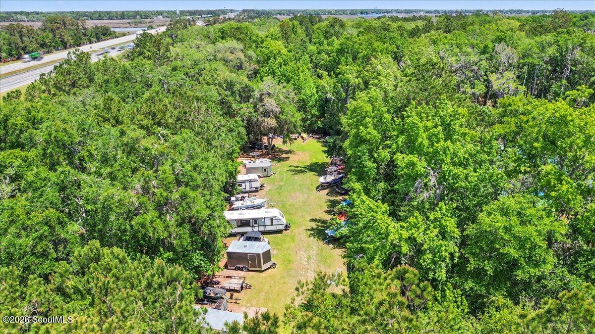 Wooded lot with a grassy clearing, RVs, boats, and trailers, viewed from above.