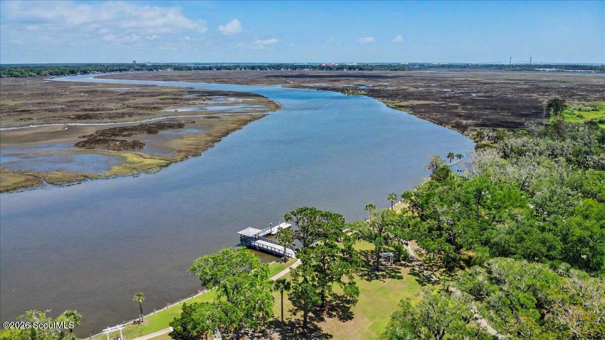 Aerial waterfront view of a tidal marsh and winding waterway, with a dock and tree-lined property.