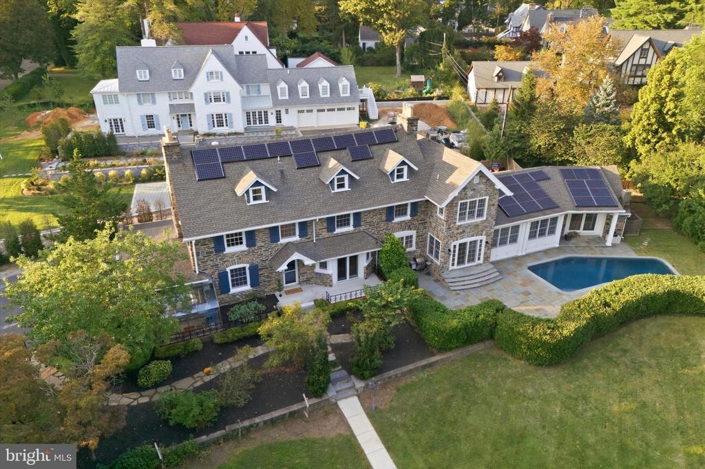 Aerial view of a stone house with rooftop solar panels, a pool, and landscaped grounds.
