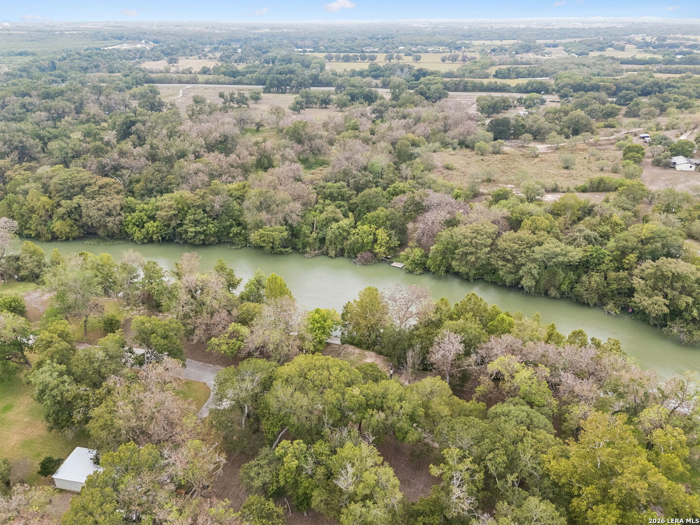 Aerial view of a wooded property along a winding river, with scattered clearings and small buildings.