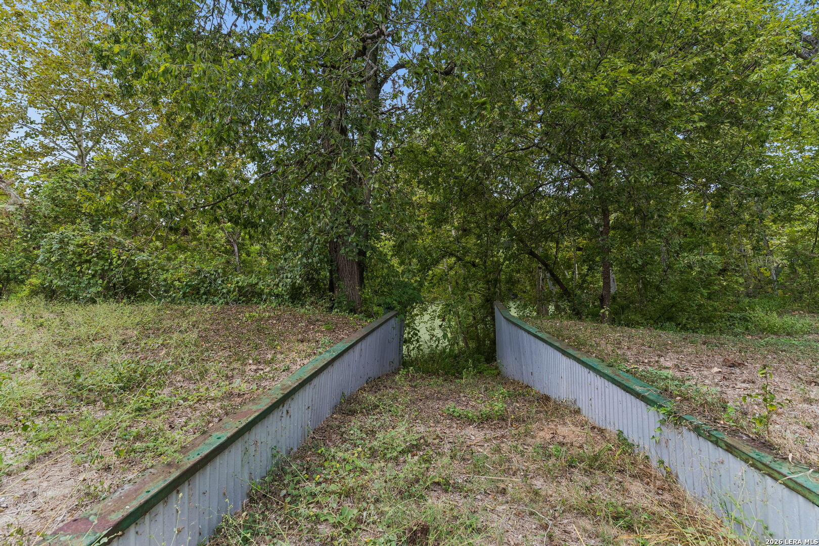 Wooded path with low-sided walkway leading toward water.