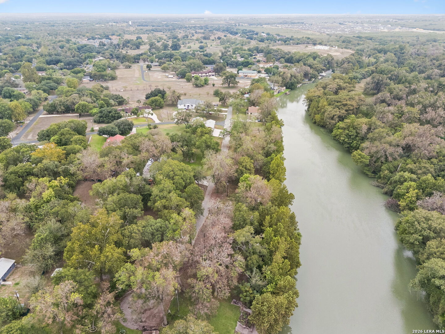 Aerial view of a tree-lined river beside homes and wooded lots.