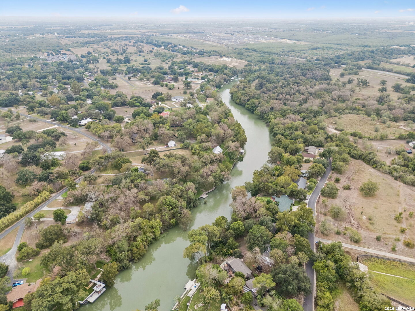Aerial view of homes along a winding river, with wooded banks and surrounding countryside.