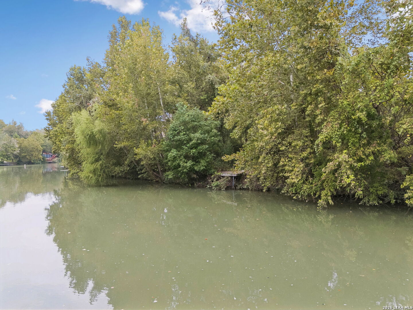 Calm water borders a wooded shoreline with autumn foliage and a small landing.