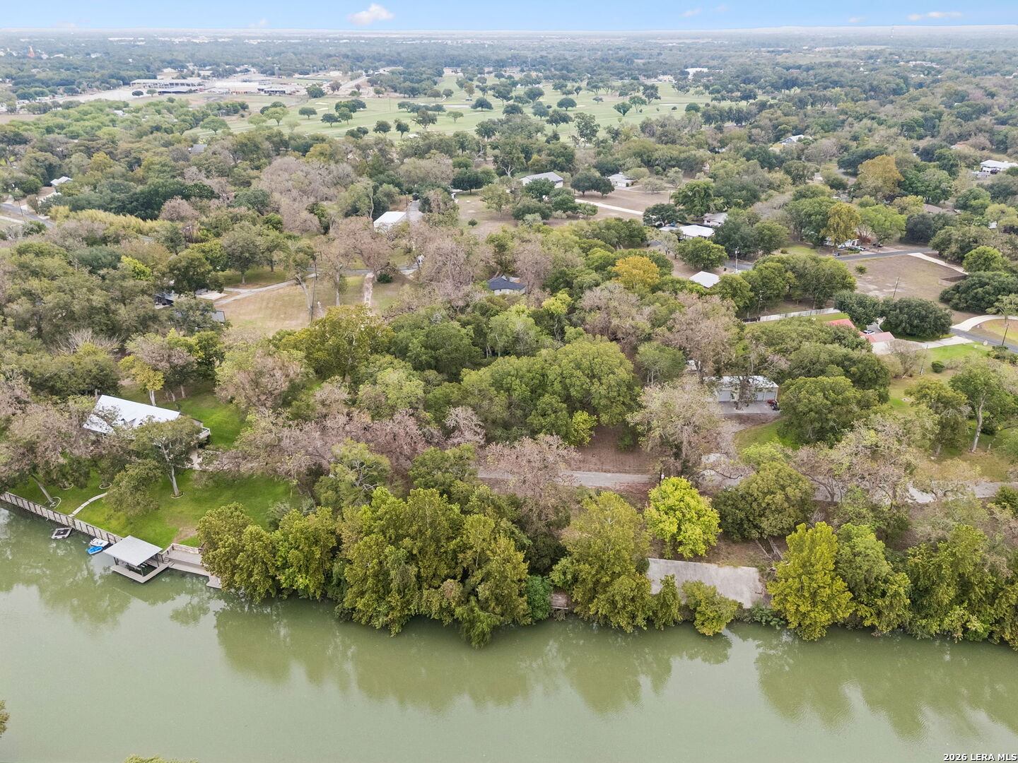 Aerial view of a wooded waterfront property with a dock and homes along the shoreline.