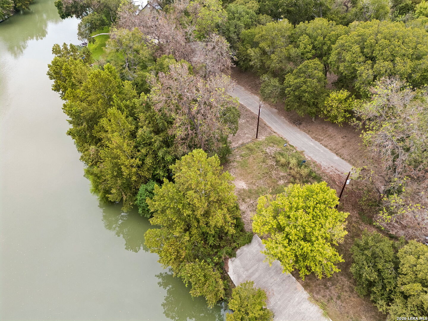 Aerial view of a wooded riverfront lot with a cleared area and paved access road.