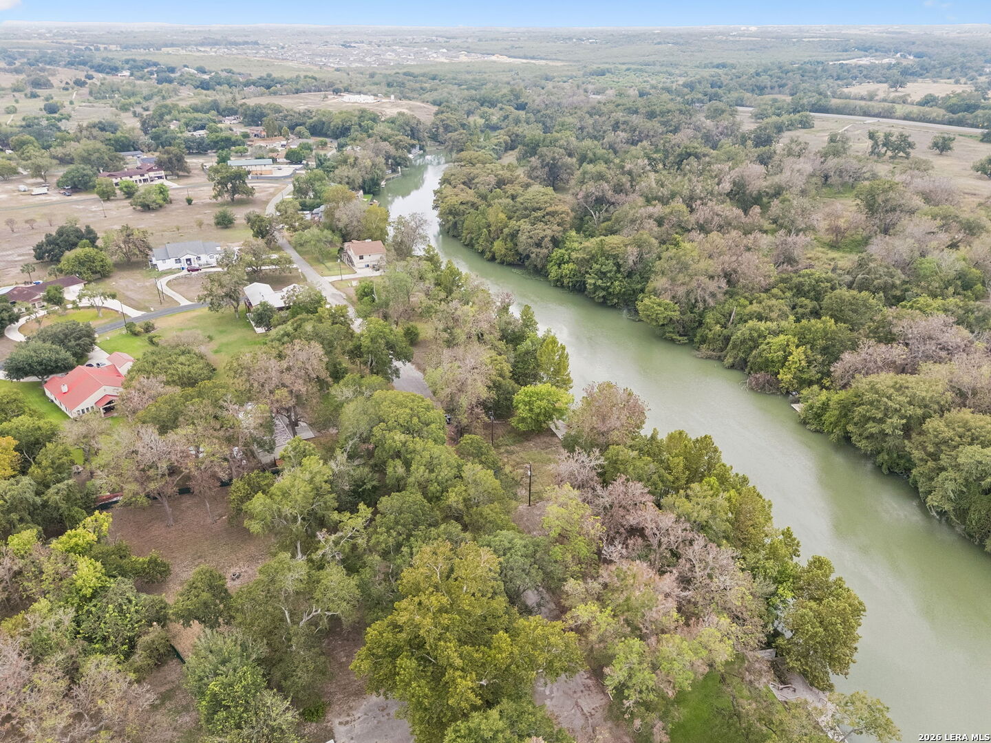 Aerial view of a winding river bordered by trees, homes, and yards.
