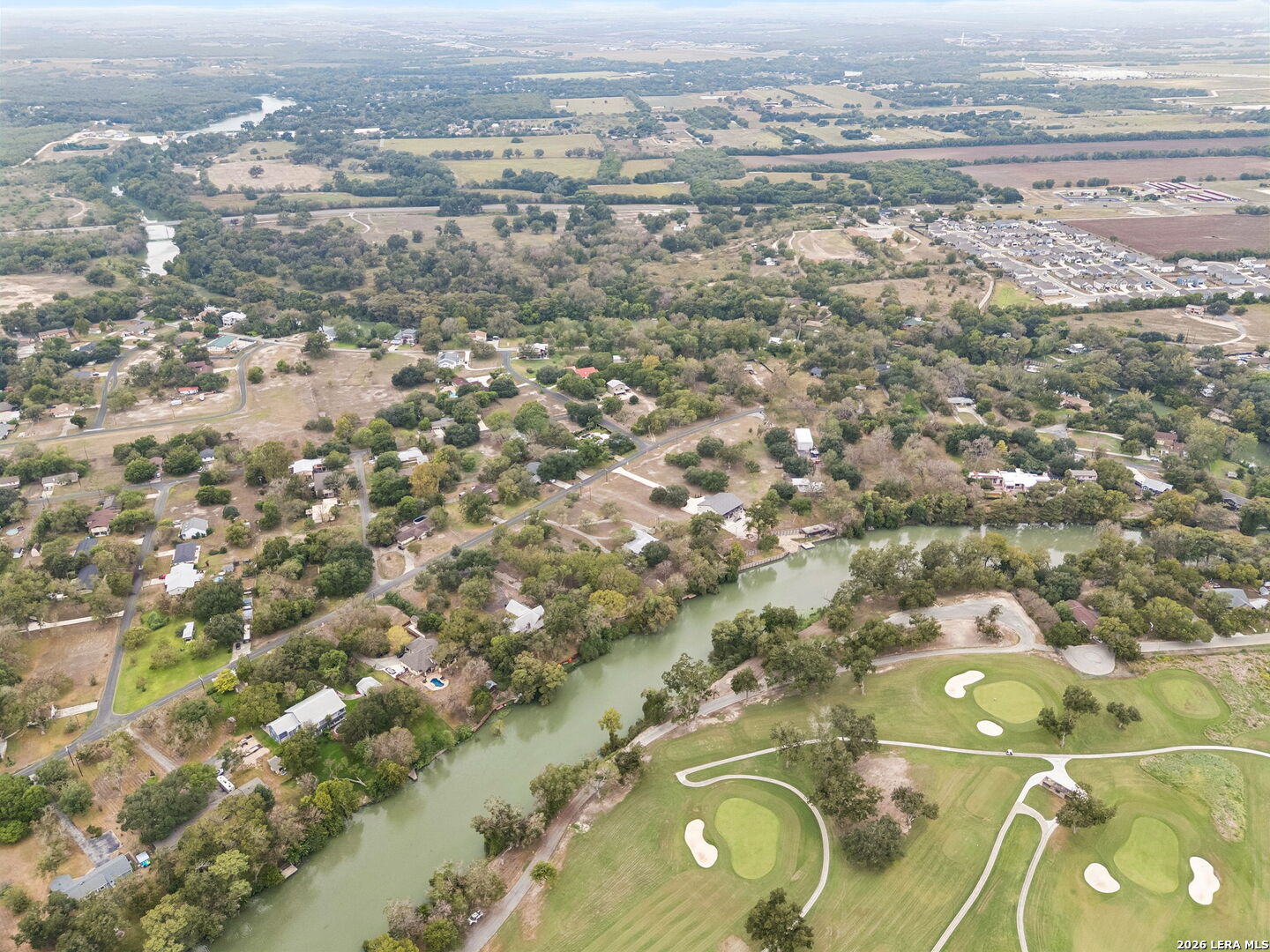 Aerial view of homes beside a winding river and golf course with sand bunkers.
