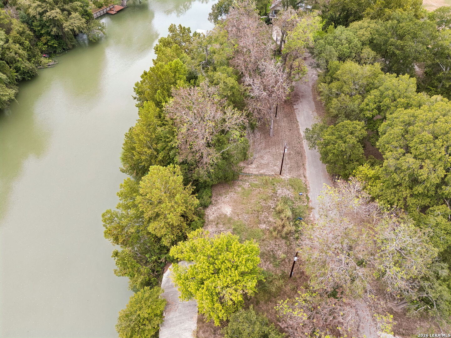 Aerial view of a wooded riverfront lot with a cleared lane and small dock.
