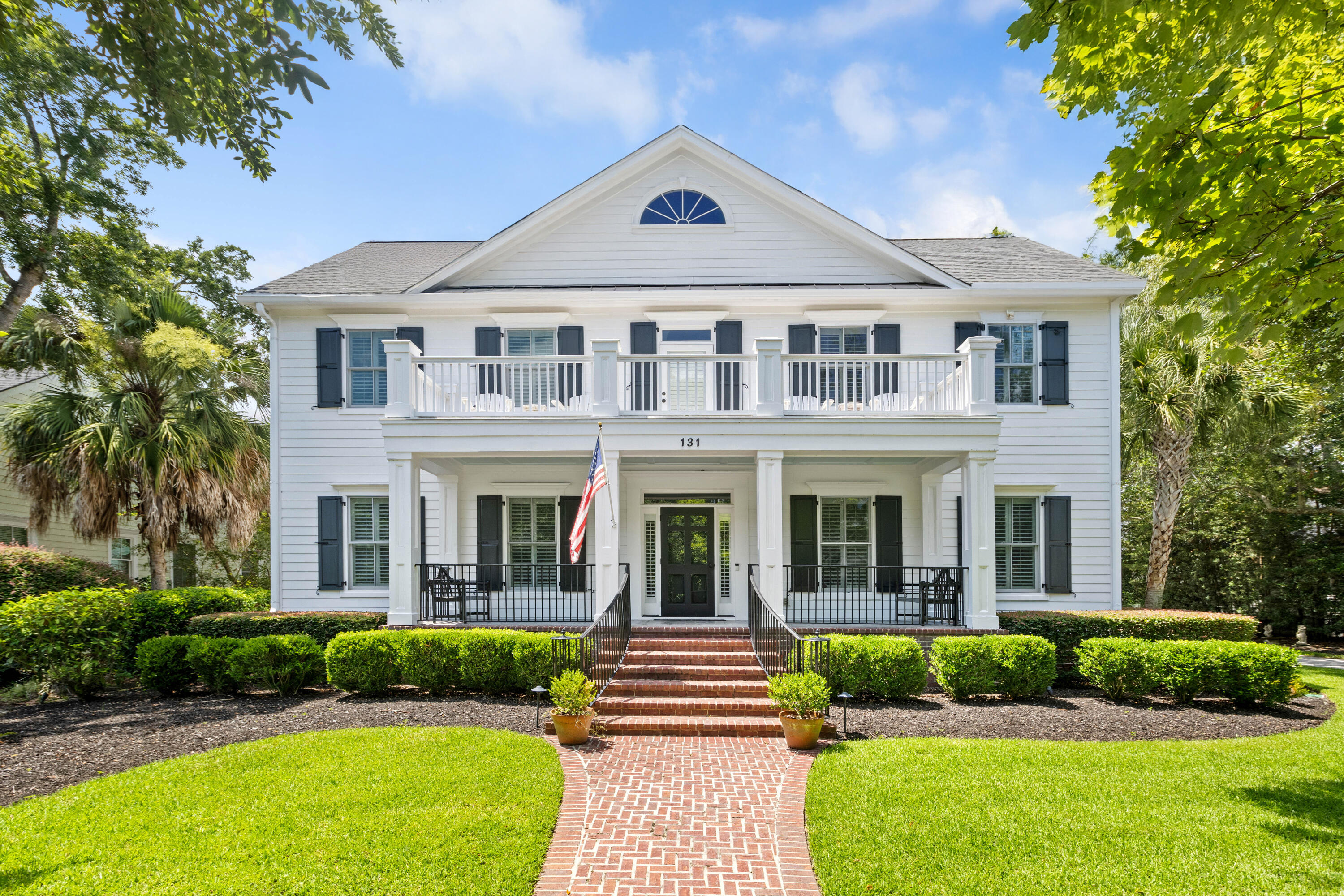 White two-story home with dark shutters, double porches, brick steps, and a landscaped front lawn.