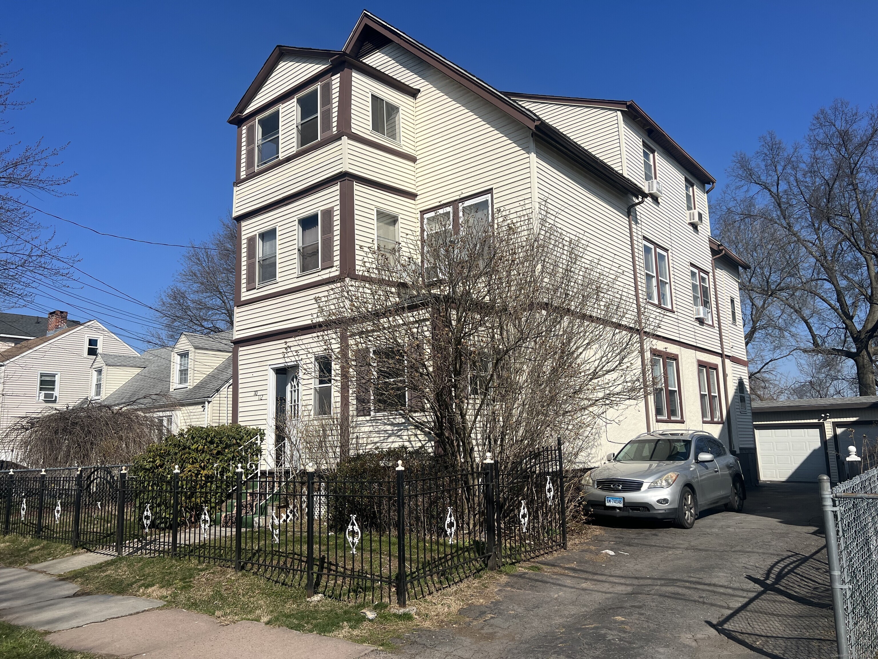 Three-story cream-sided residence with dark trim, a fenced yard, and a driveway beside a detached garage.