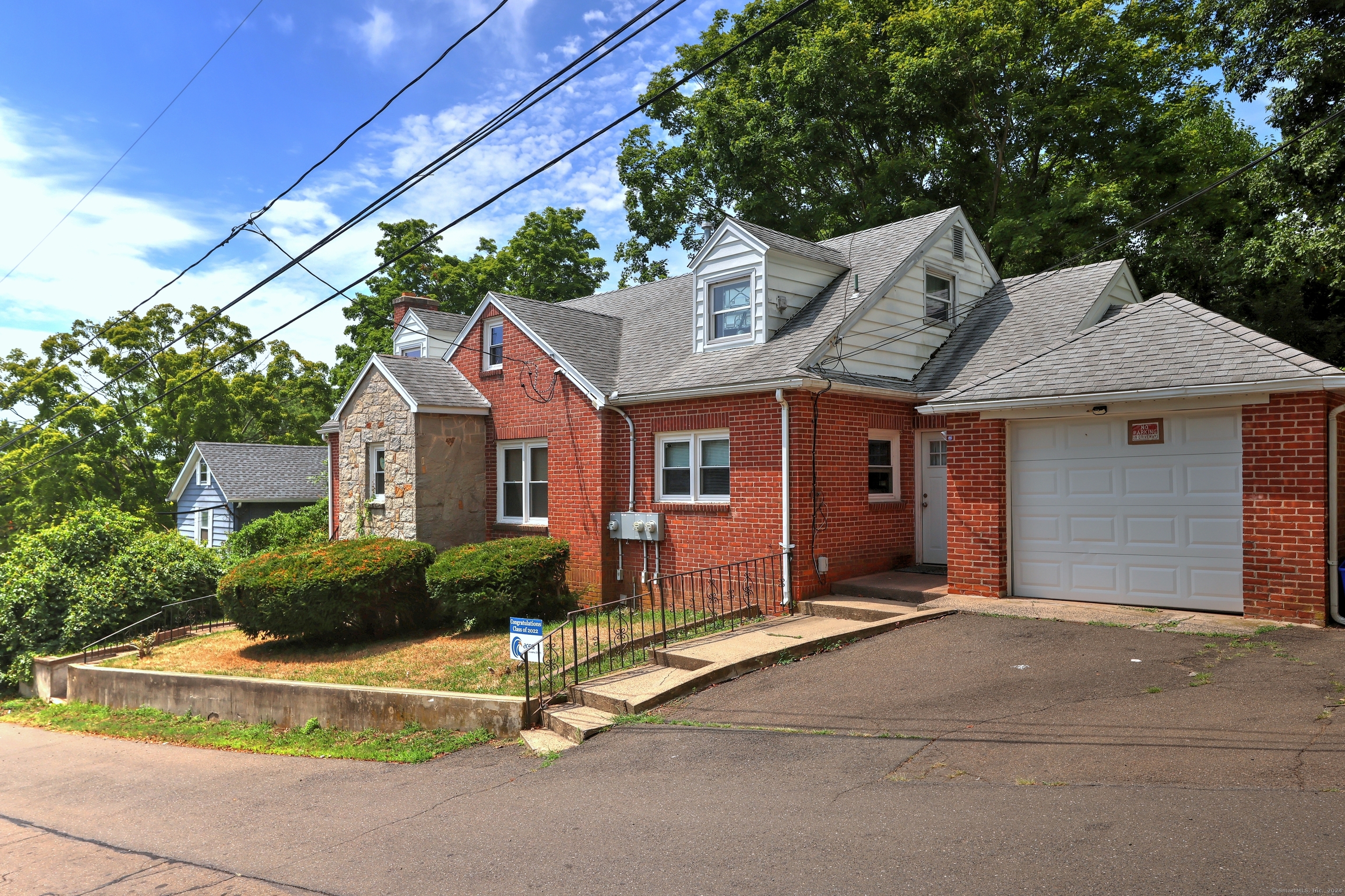 Red brick house with a stone entry, white dormers, attached garage, and wide paved driveway.