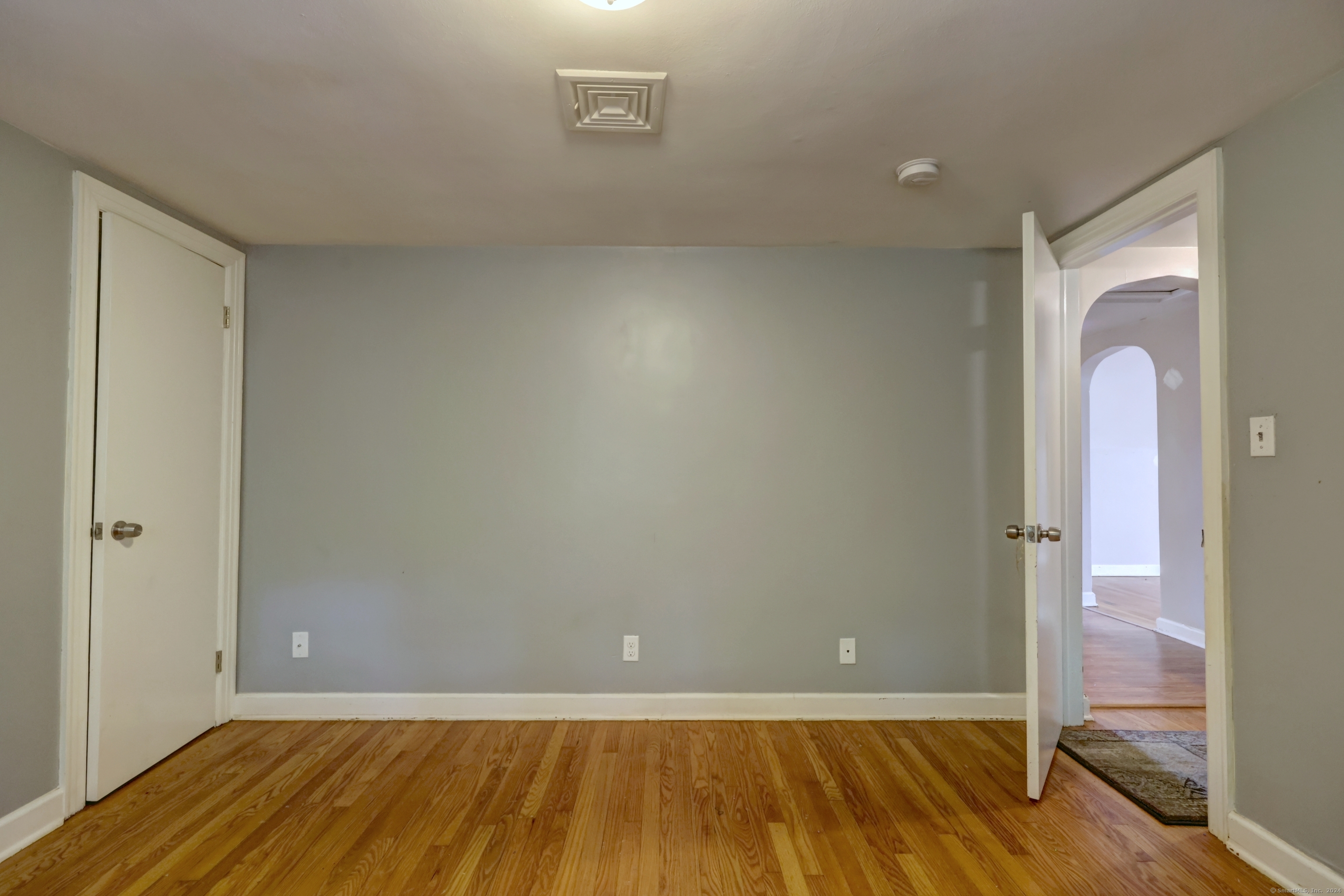 Empty room with gray walls and hardwood floors, viewed toward two open doorways.