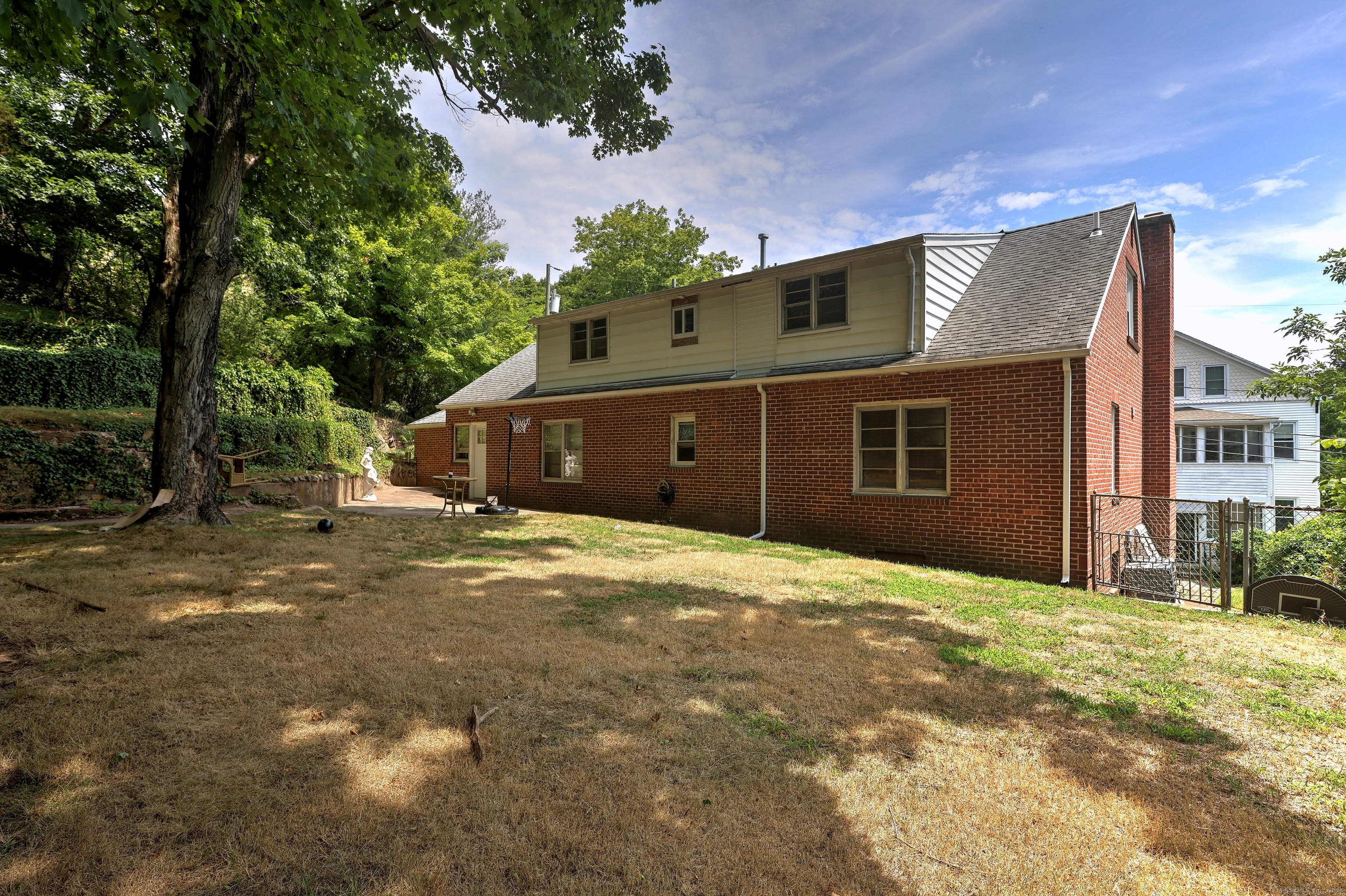 Rear of a two-story brick home with light siding, a dry backyard, and mature shade trees.