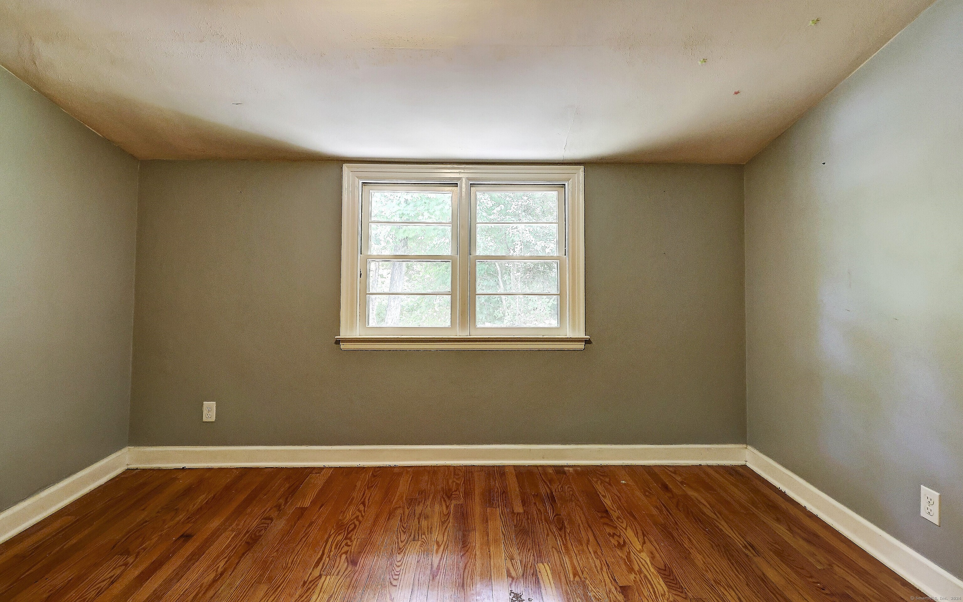 Empty room with hardwood floors and a centered double window.
