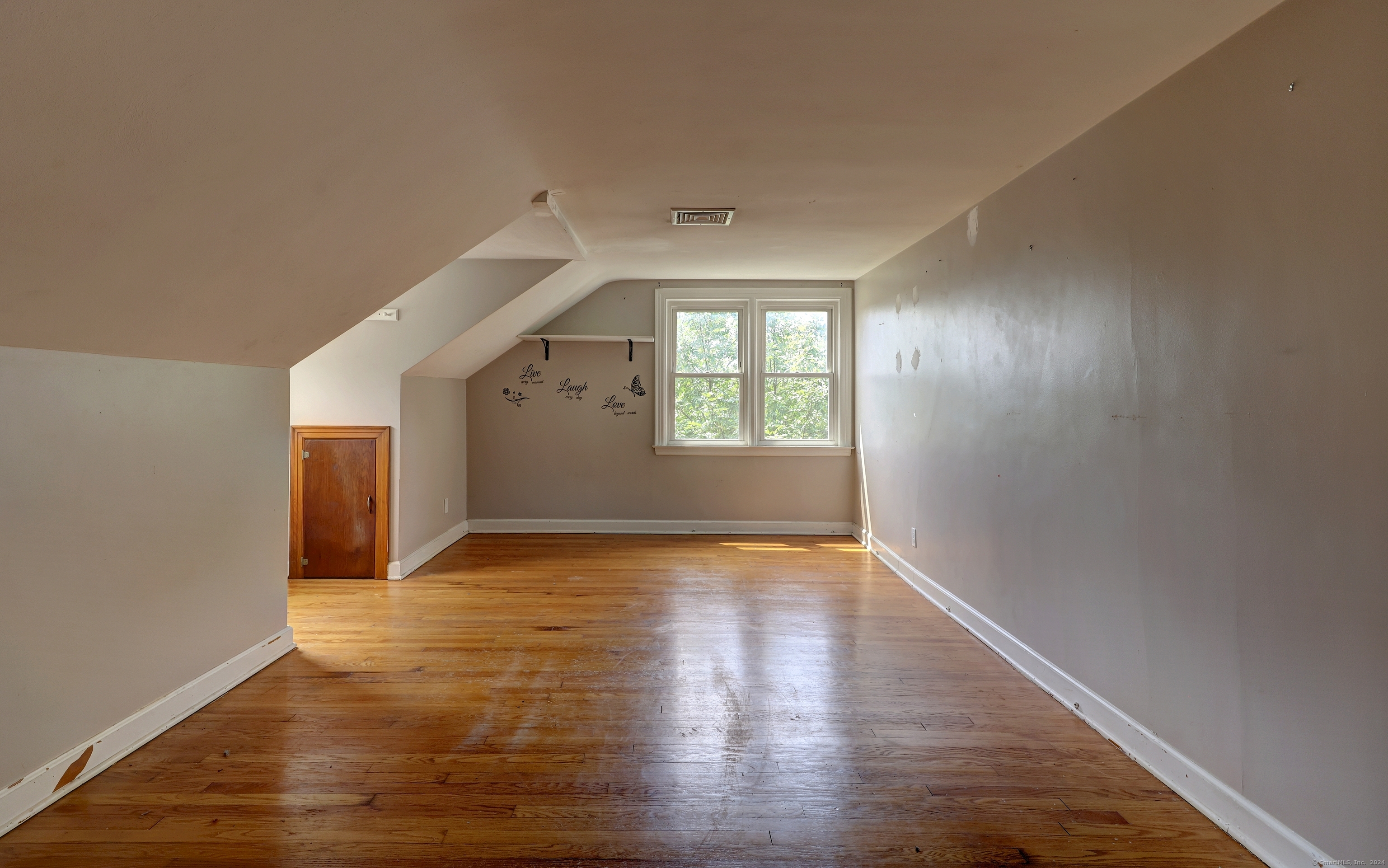 Vacant attic room with sloped ceilings, hardwood floors, and two windows.