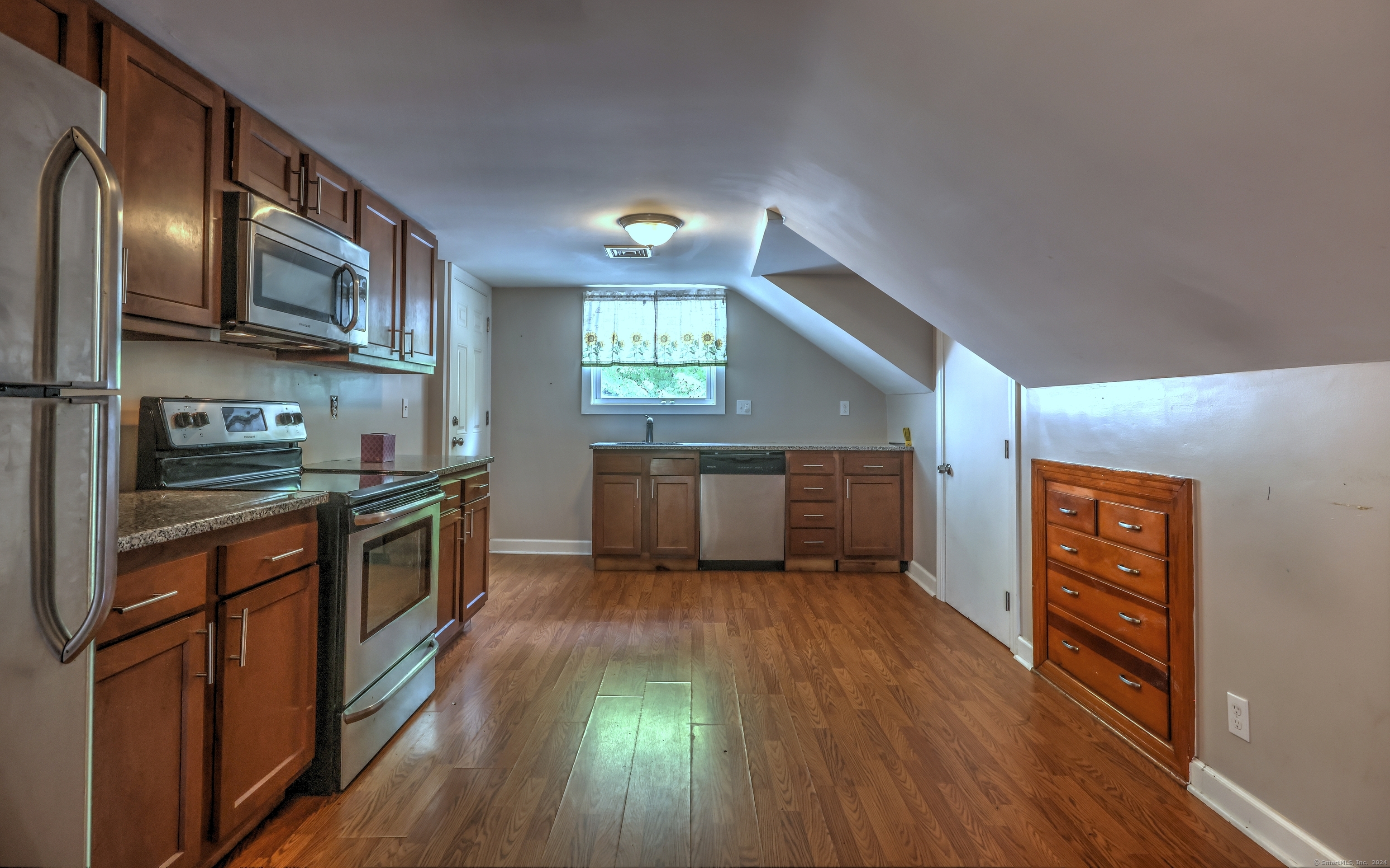 Kitchen with wood cabinetry, stainless steel appliances, hardwood floors, and a sloped ceiling.