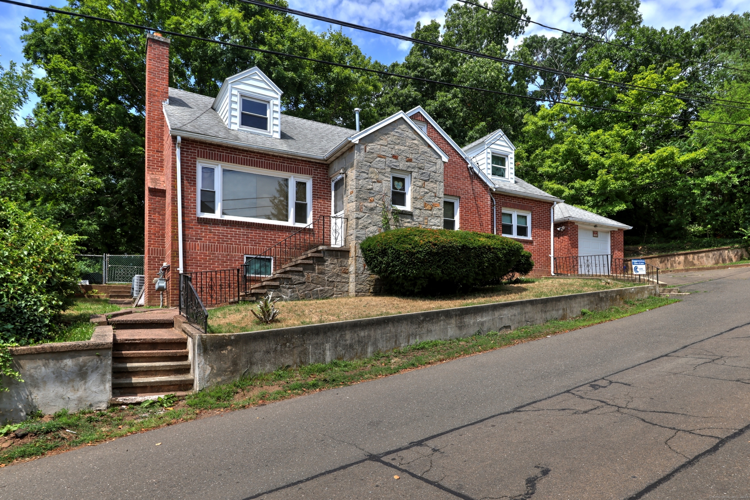 Red brick and stone house with front steps, dormer windows, and an attached garage.