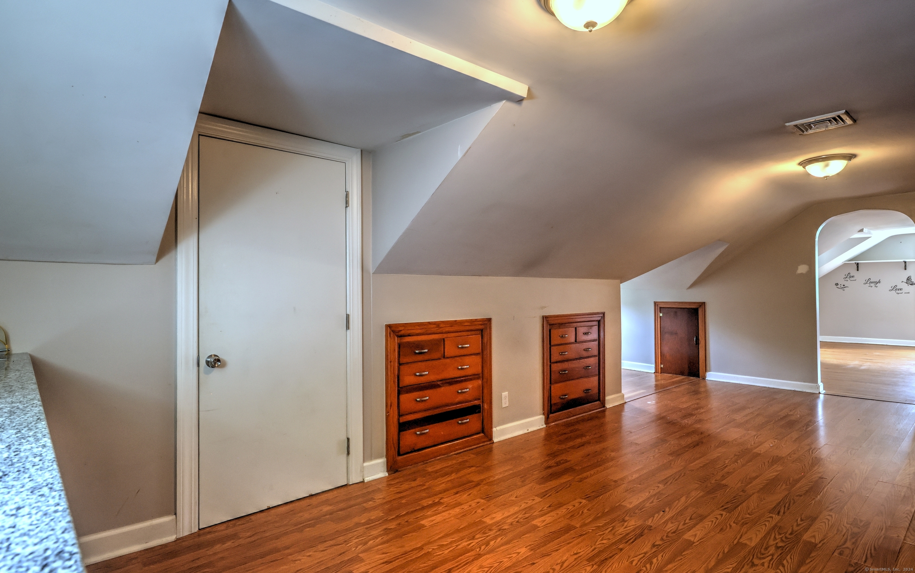 Upper-level room with sloped ceilings, hardwood floors, and built-in wooden dressers.