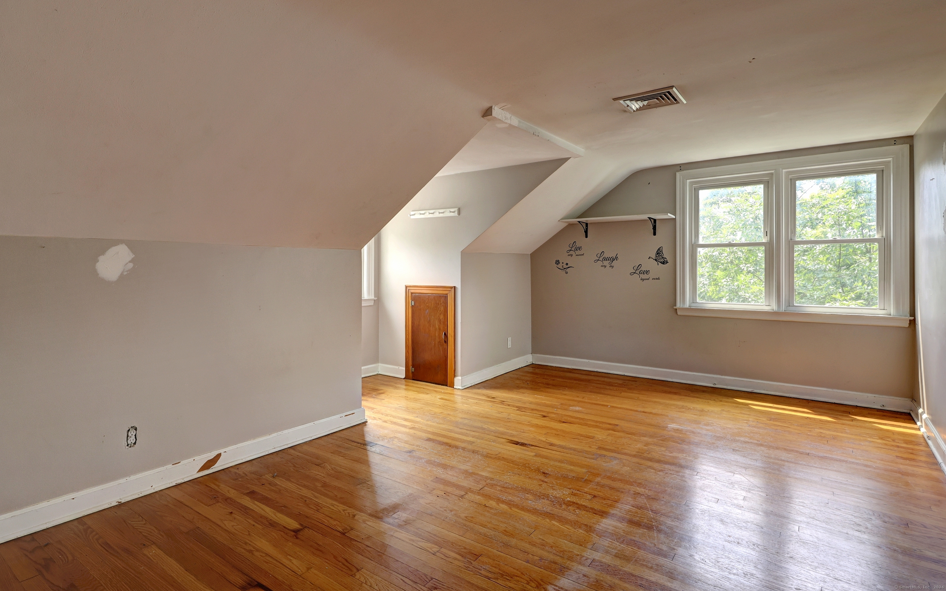 Vacant upper-floor room with sloped ceilings, hardwood floors, and two large windows.