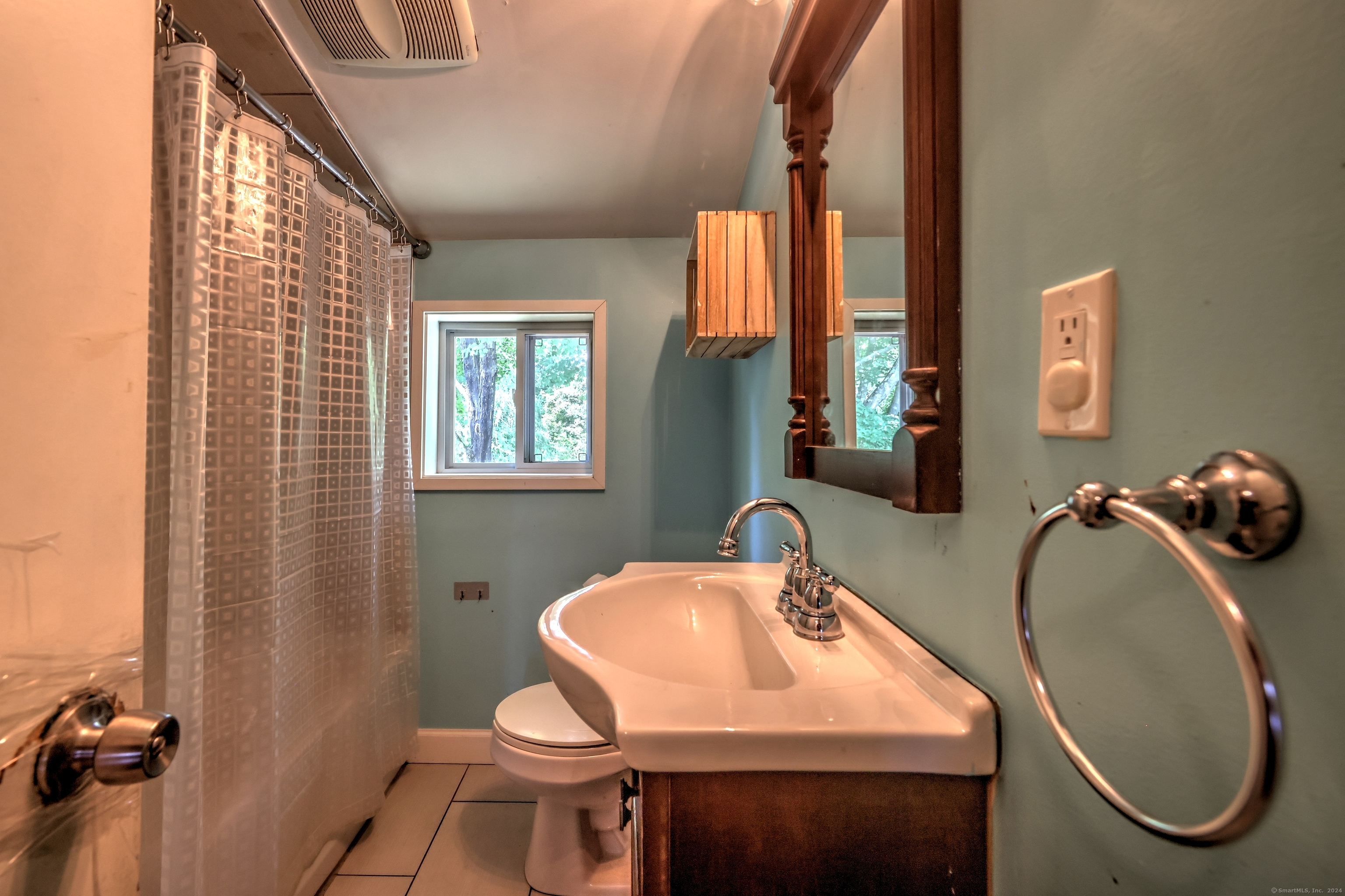 Bathroom with a white sink and dark wood vanity, shower curtain, and window overlooking trees.