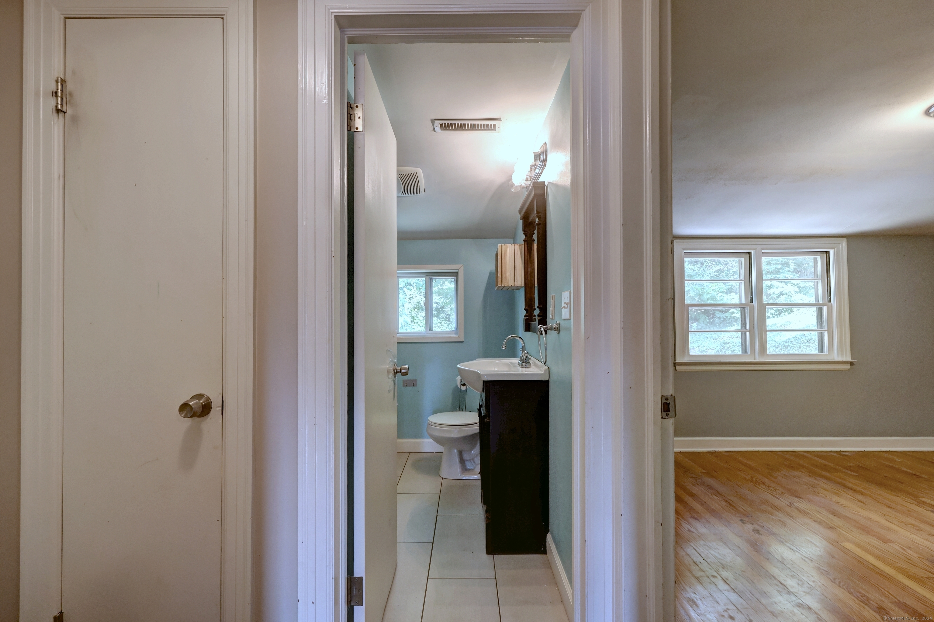 Bathroom with blue walls, tiled floor, and dark vanity, viewed from an adjoining hardwood-floored room.