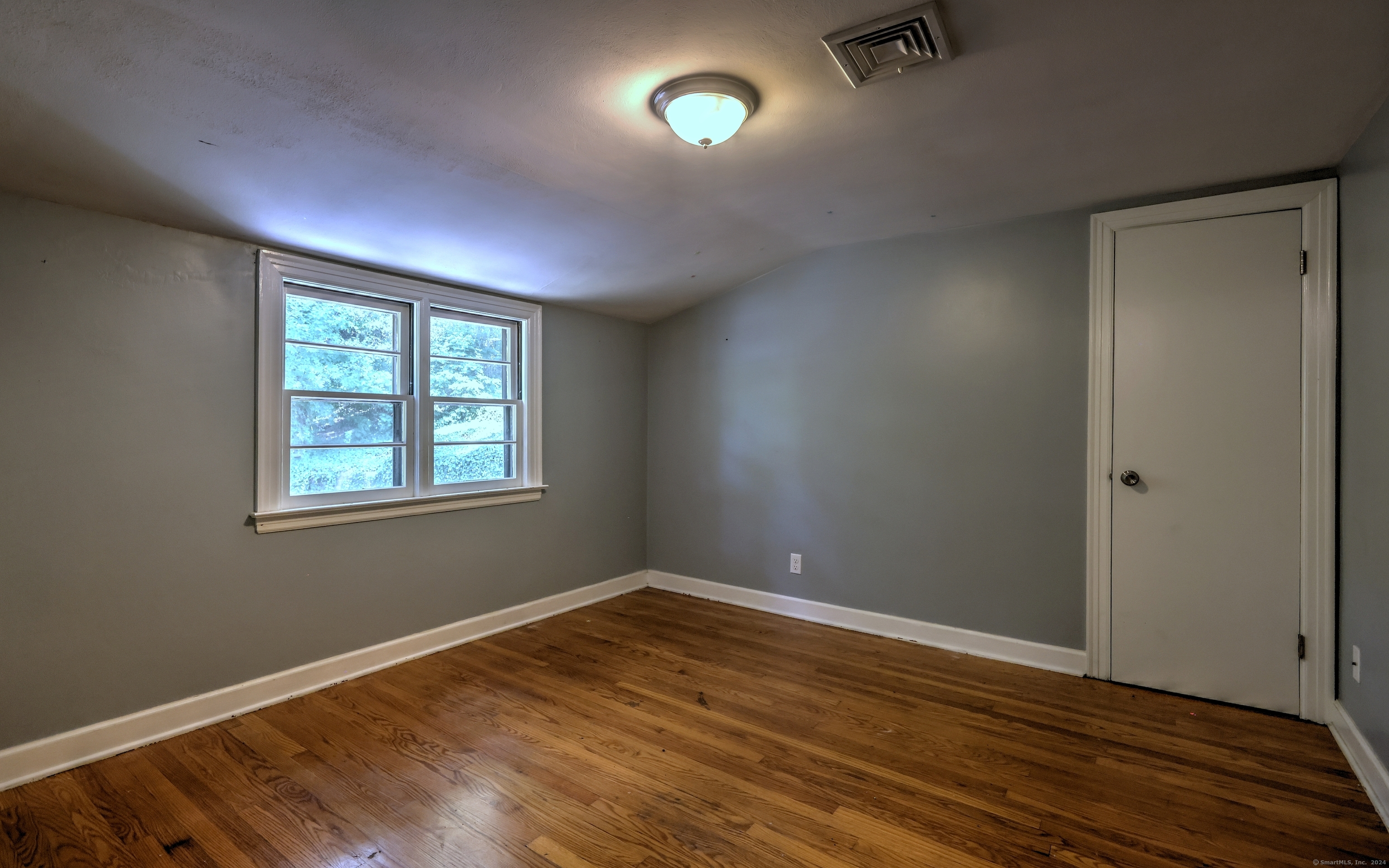 Empty room with hardwood floors, gray walls, and two windows.