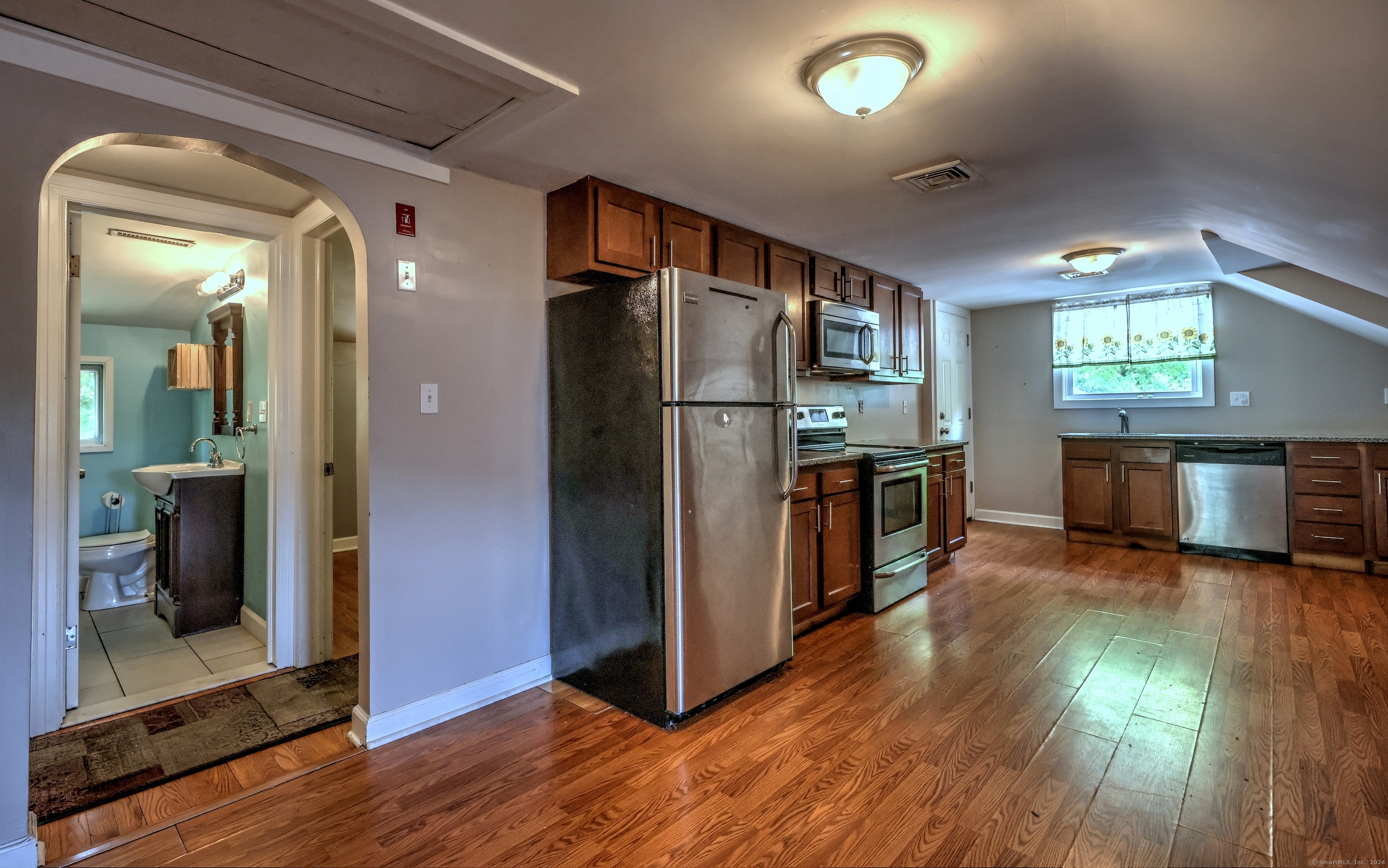 Kitchen with dark wood cabinets, stainless steel appliances, hardwood floors, and an arched doorway to a bathroom.