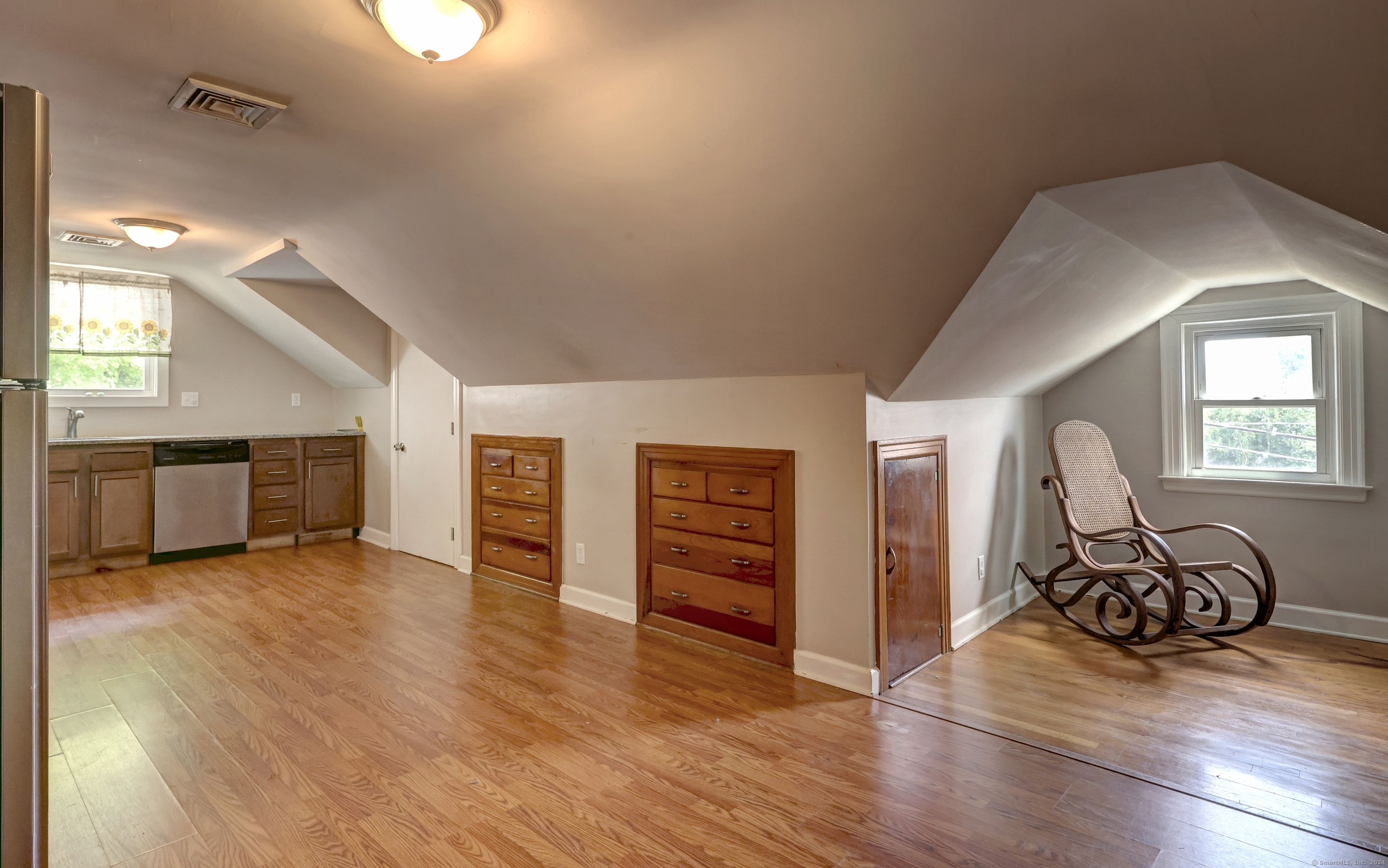 Finished attic with a small kitchenette, built-in dressers, hardwood floors, and a rocking chair by the window.