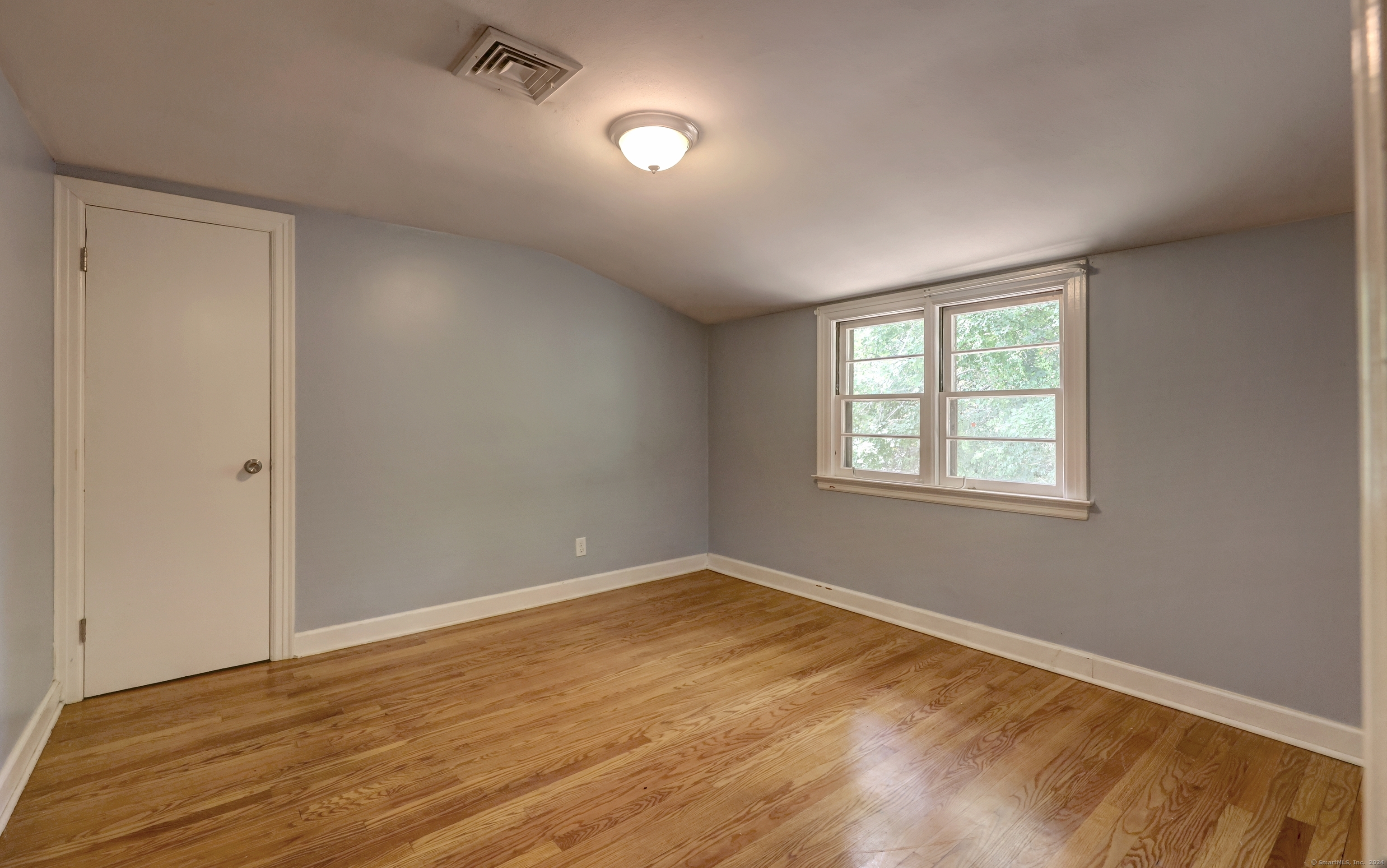 Unfurnished room with hardwood floors, gray walls, and a double window overlooking trees.